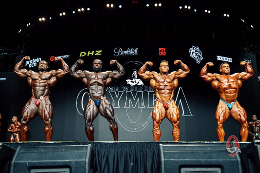 Four elite Men's Open bodybuilders posing side by side in a front double-biceps comparison at the 2026 Mr. Olympia