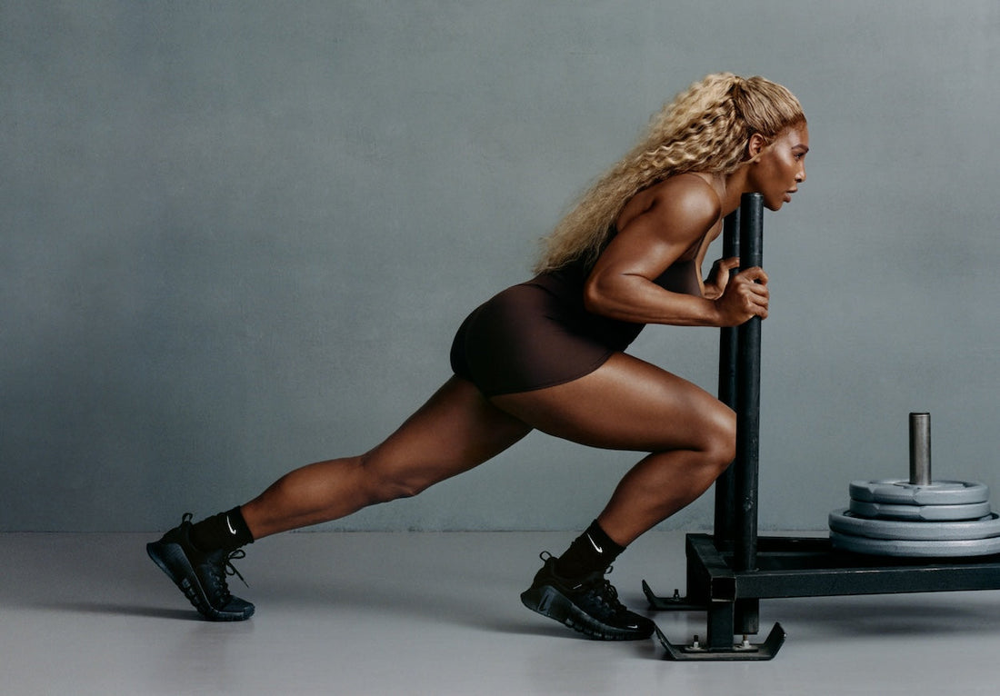 Serena Williams pushing a weighted training sled in a dark studio, demonstrating lower-body power