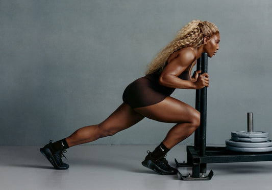 Serena Williams pushing a weighted training sled in a dark studio, demonstrating lower-body power