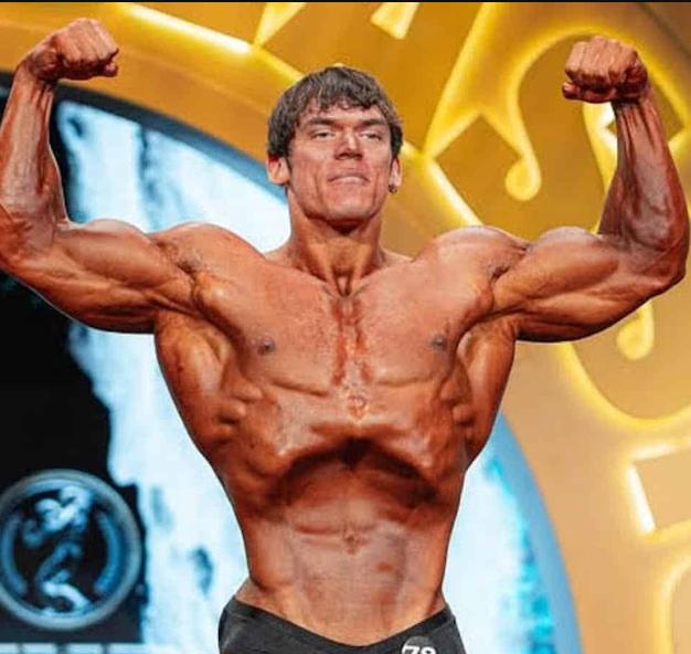 Sam Sulek hitting a front double-biceps pose on the 2026 Arnold Classic stage with broad delts