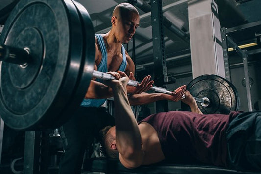 Powerlifter bench pressing a loaded barbell with an attentive spotter