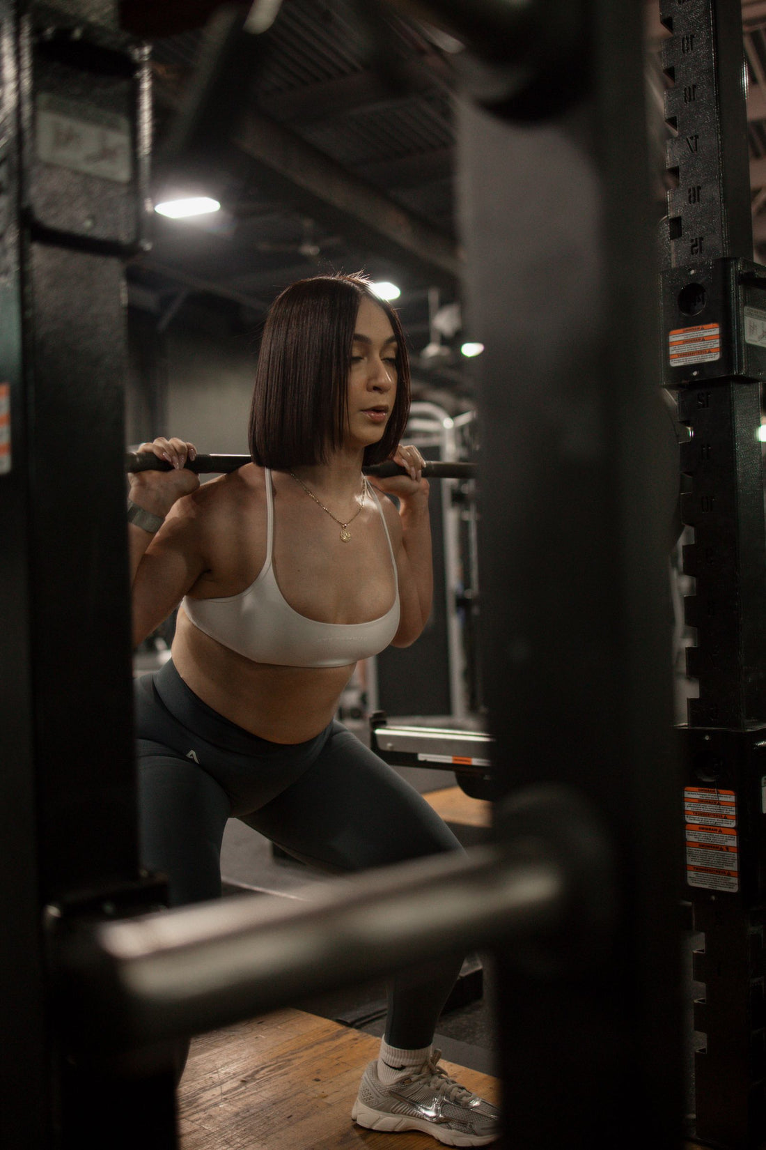 Woman performing a controlled barbell squat inside a weight-training gym