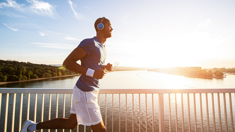Runner wearing headphones on a sunny bridge during a long endurance run