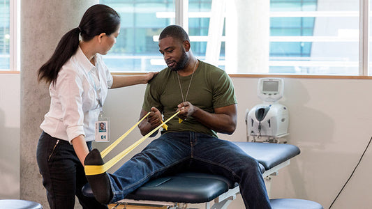 Physiotherapist guiding a seated athlete through resistance-band ankle exercise