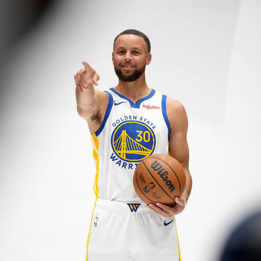 Stephen Curry holding a basketball in a Golden State Warriors jersey at 2025-26 media day