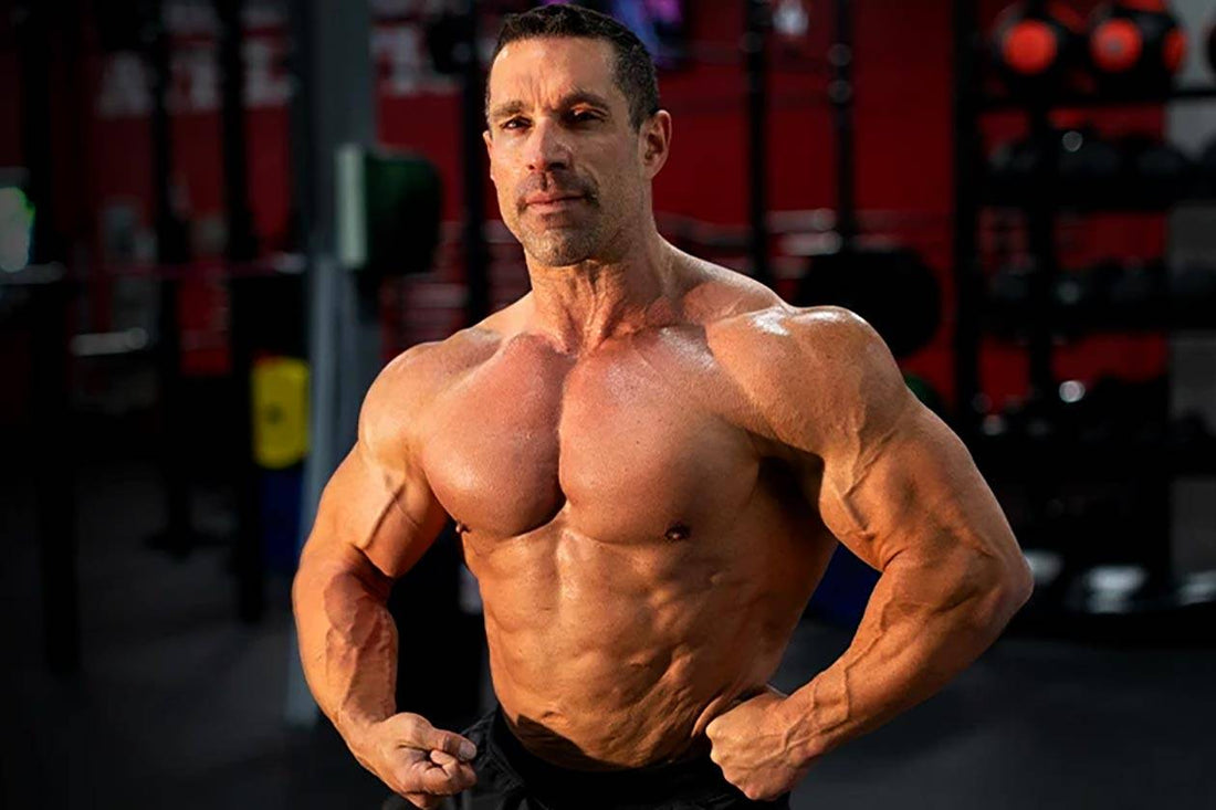 Greg Doucette flexing in a gym, showing the muscular physique built during his bodybuilding career