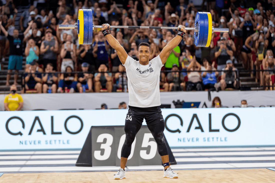 Gui Malheiros holding a loaded barbell overhead at a CrossFit competition