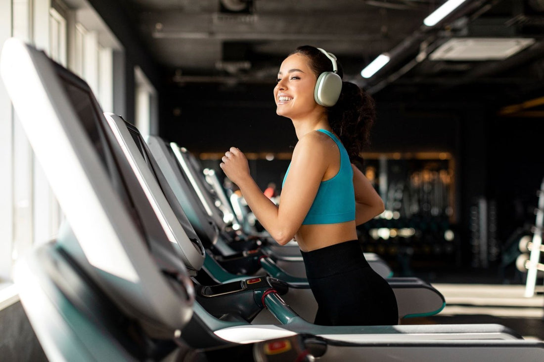 Woman smiling while running on a treadmill with headphones in a modern gym