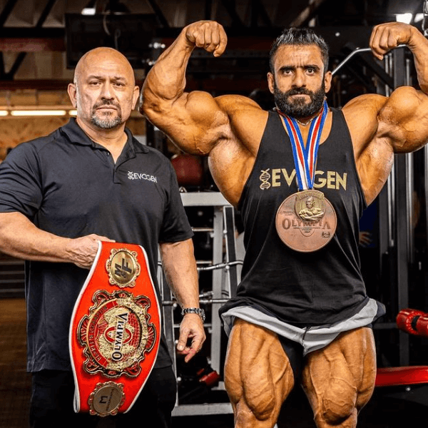 Hadi Choopan holding the 2022 Mr. Olympia trophy while coach Hany Rambod celebrates beside him on stage