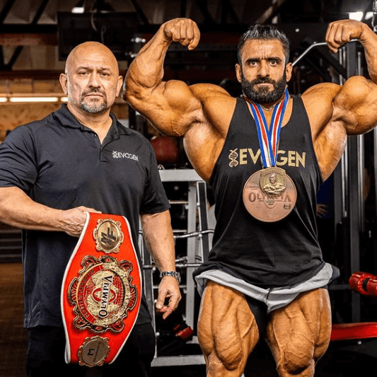 Hadi Choopan holding the 2022 Mr. Olympia trophy while coach Hany Rambod celebrates beside him on stage