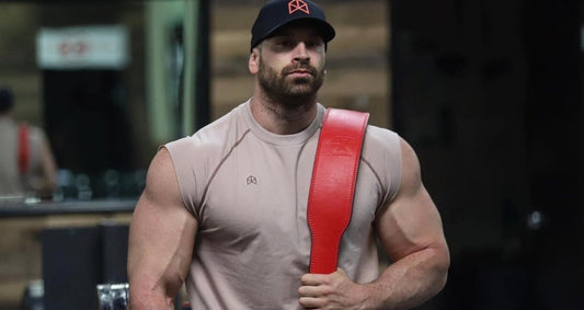Bradley Martyn in a sleeveless gym shirt holding a red lifting belt over one shoulder