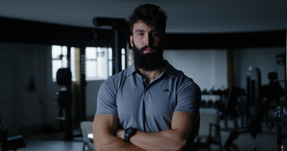 Dr. Milo Wolf in a grey polo shirt standing in a gym, dark beard and folded arms.