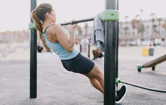 Woman doing a strict inverted row on an outdoor exercise bar, heels grounded and torso straight