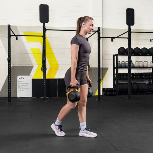 Female athlete walking in a gym with a kettlebell in each hand