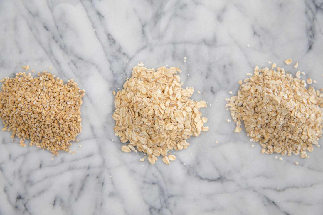 Three separate piles of steel-cut, rolled and instant oats on a pale marble surface