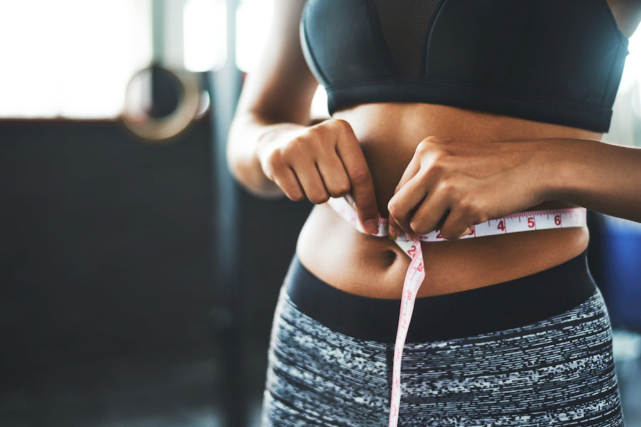 Person measuring waist circumference with a flexible tape to monitor body-composition changes