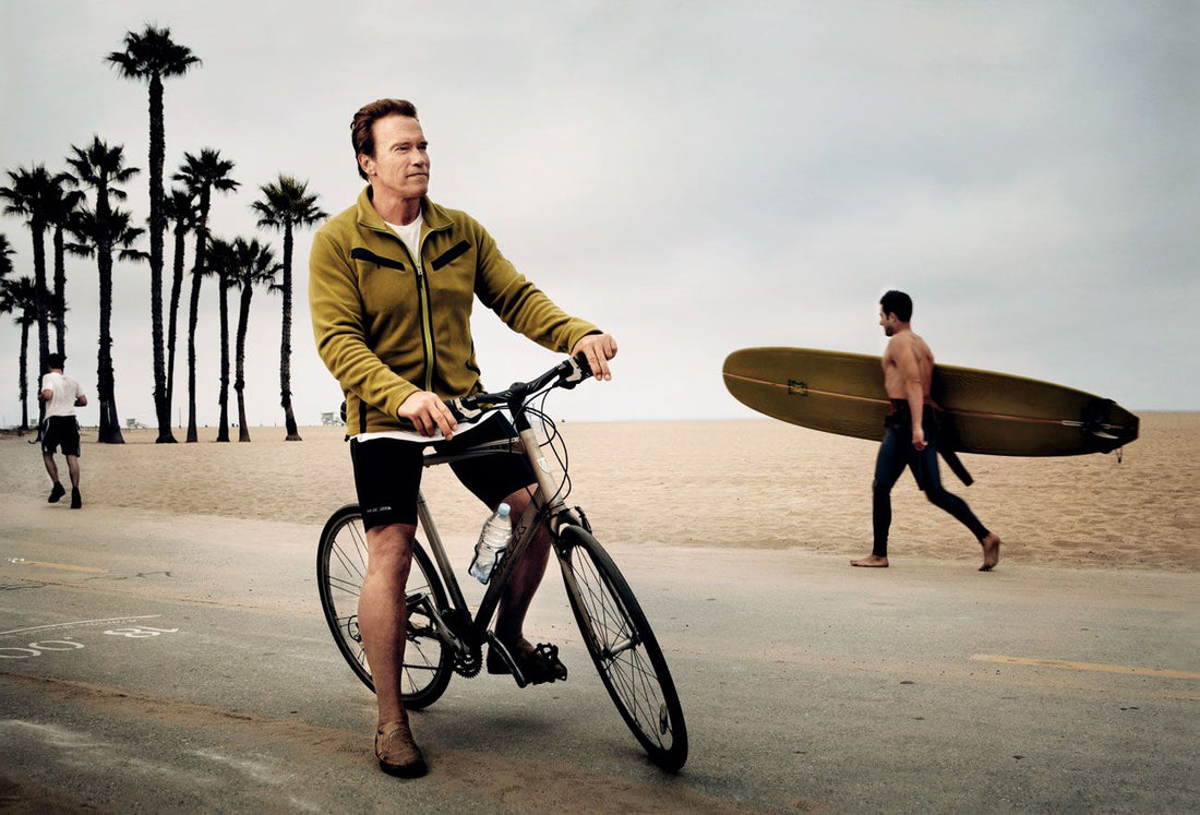 Arnold Schwarzenegger standing with a bicycle beside a California beach path