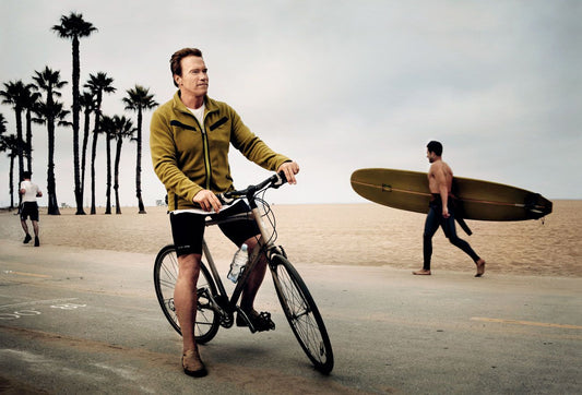 Arnold Schwarzenegger standing with a bicycle beside a California beach path