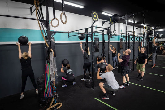 Group of functional fitness athletes performing wall-ball throws in a CrossFit gym
