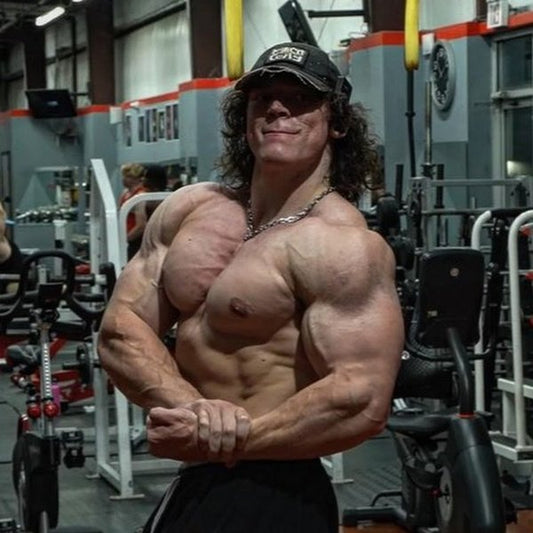 Sam Sulek posing in a commercial gym, showing muscular chest, shoulders and arms