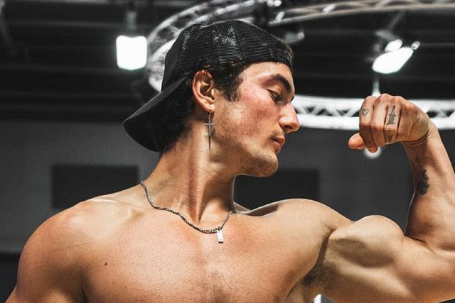 Jesse James West flexing his right biceps in a gym with clearly visible shoulder and upper-arm definition