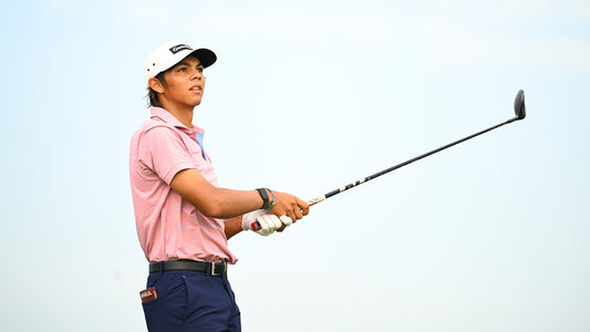 Charlie Woods follows a golf shot during the 2026 season in a pink striped polo and white TaylorMade cap