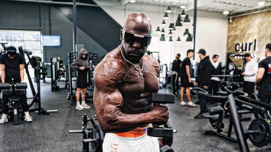 Kali Muscle lifting a dumbbell in a busy gym
