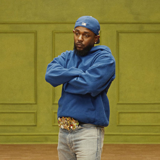 Kendrick Lamar wearing a blue hoodie and backwards cap in a performance scene