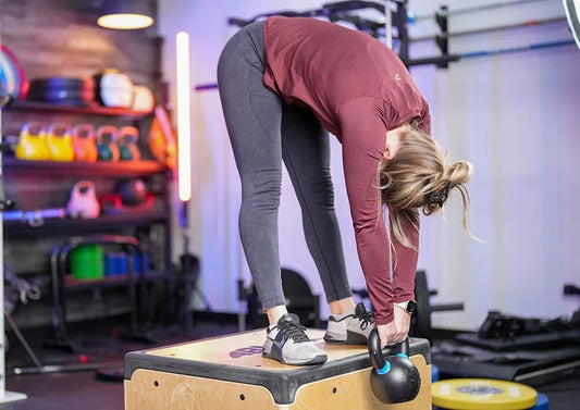 Athlete practicing a light kettlebell Jefferson curl on a stable plyometric box in a gym