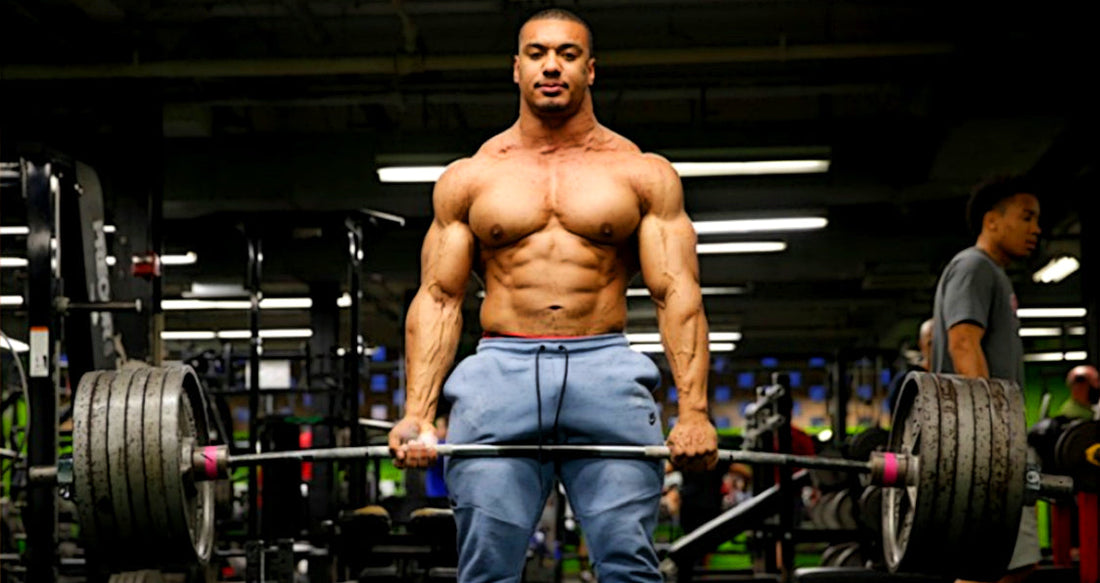 Larry Wheels shirtless gripping a loaded barbell in a gym
