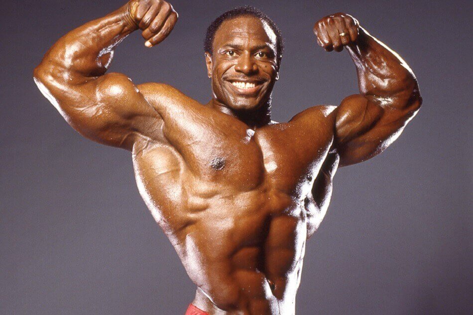 Lee Haney smiling in a front double-biceps pose with broad shoulders, developed lats and a narrow waist