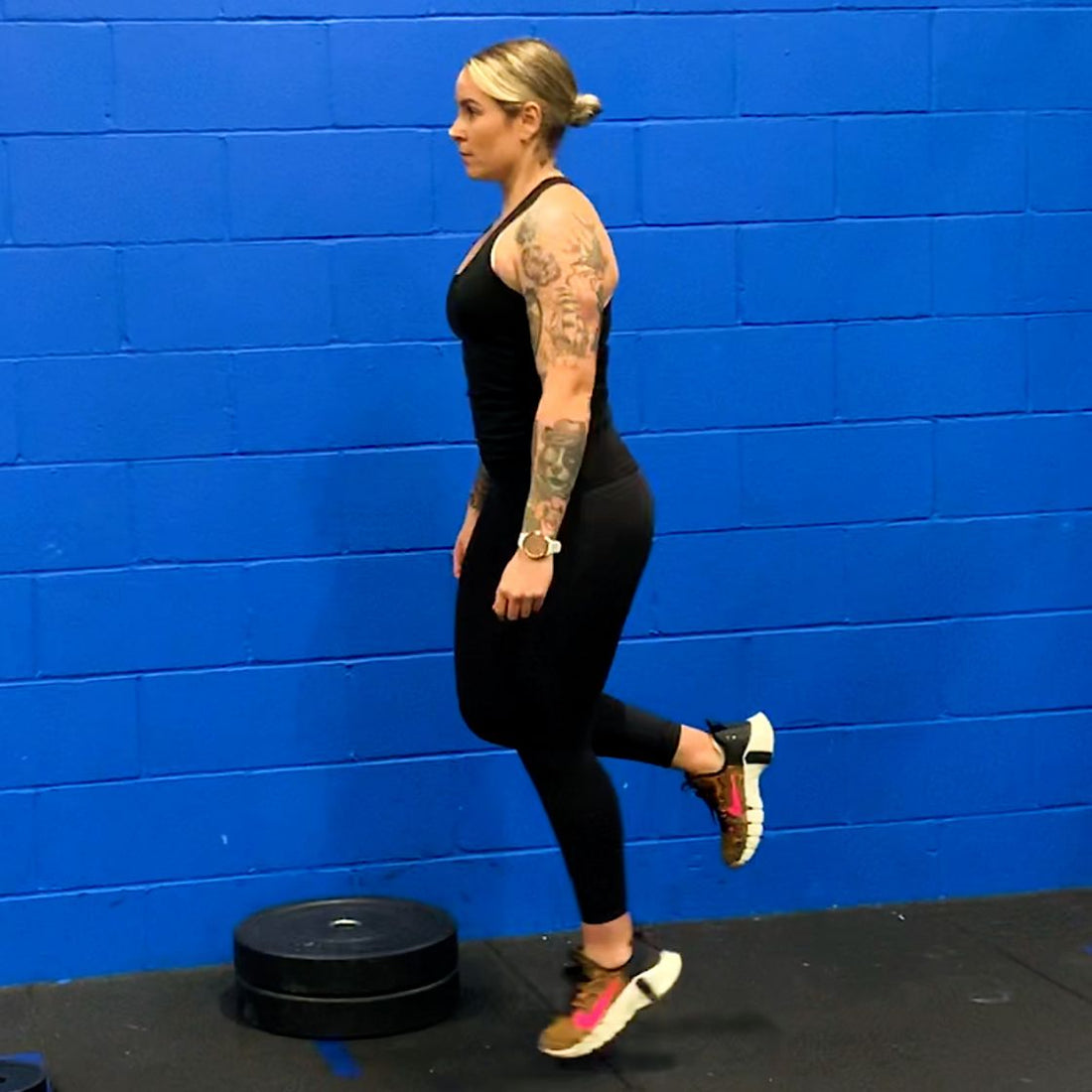 Woman performing a strict single-leg calf raise in a gym against a blue wall