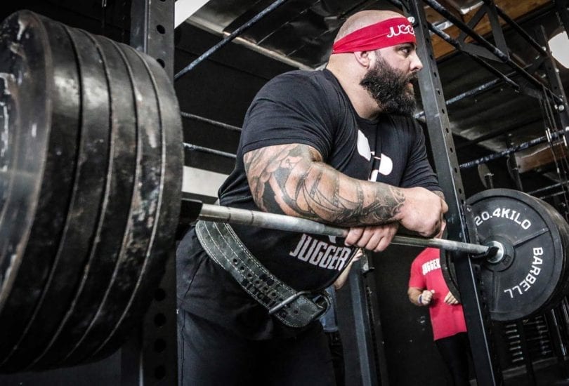 Strength athlete leaning on a loaded barbell during a pause between heavy gym sets
