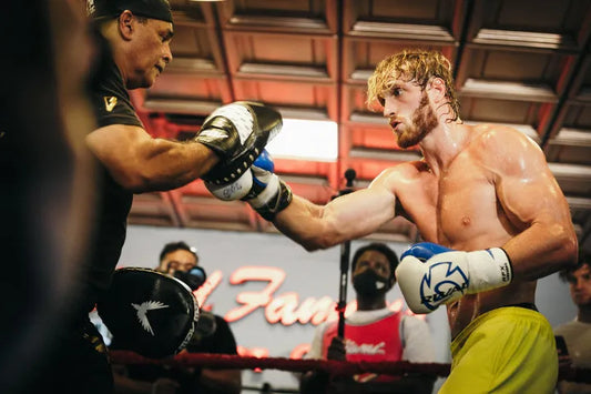 Logan Paul shirtless doing boxing mitt work with a trainer in a Miami gym