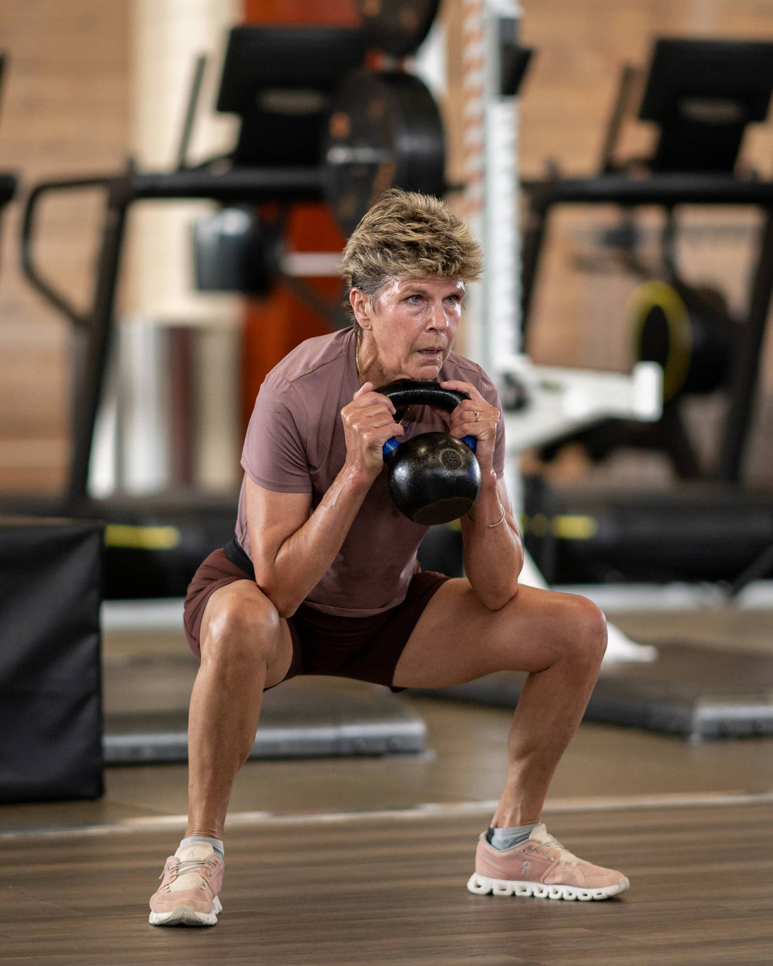 Older woman performing a loaded kettlebell squat in a gym