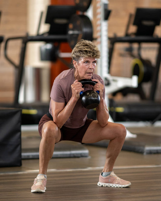 Older woman performing a loaded kettlebell squat in a gym