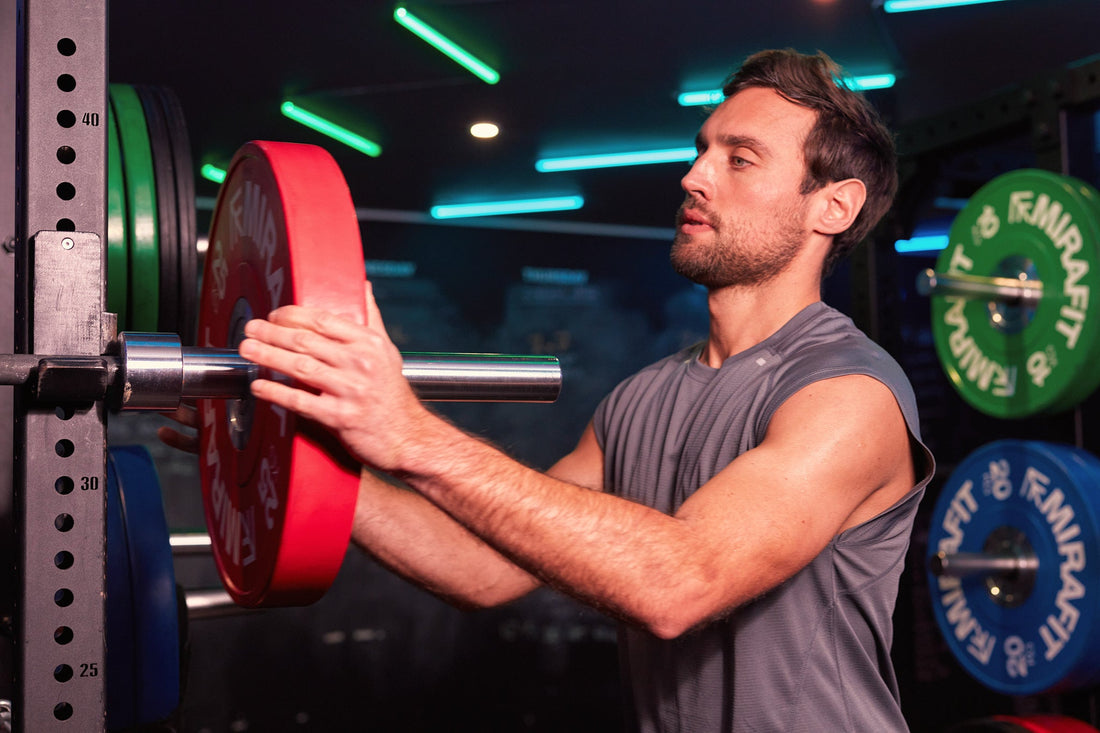 Man adding a weight plate to a barbell in a squat rack to illustrate progressive overload