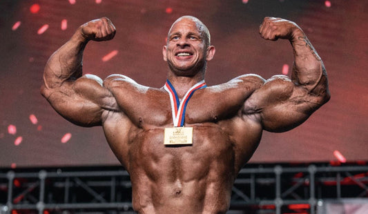 Michal Krizo lifting his Pittsburgh Pro 2026 winner's trophy on a bodybuilding stage