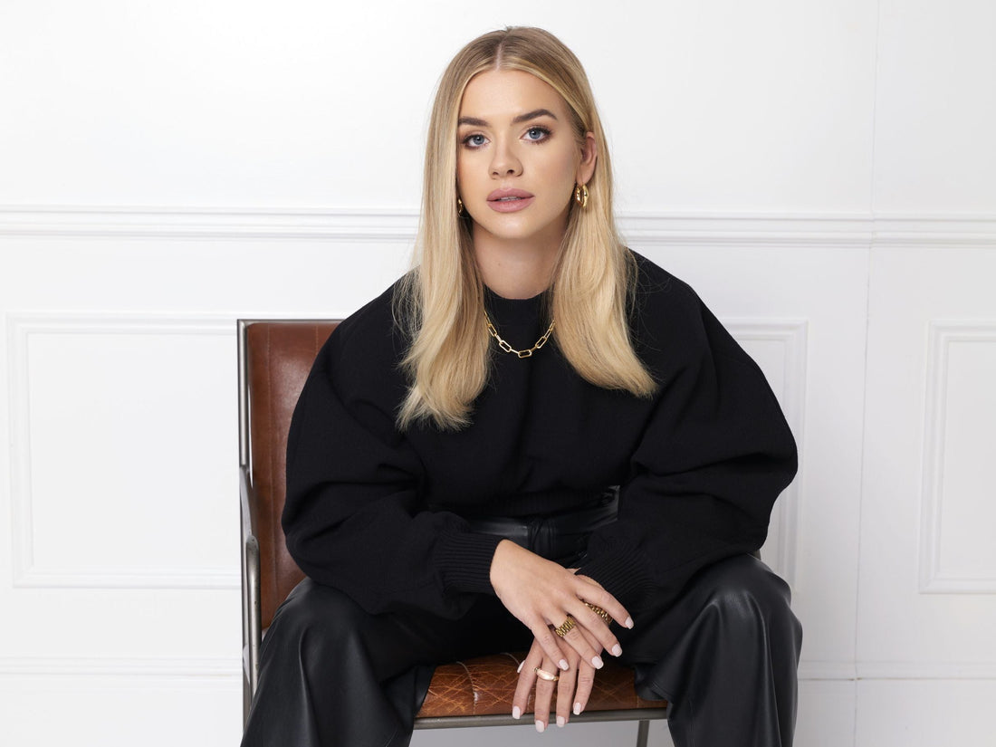 Grace Beverley seated in black clothing against a light studio background