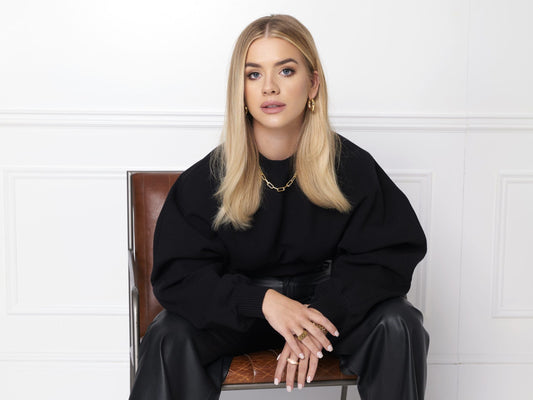 Grace Beverley seated in black clothing against a light studio background