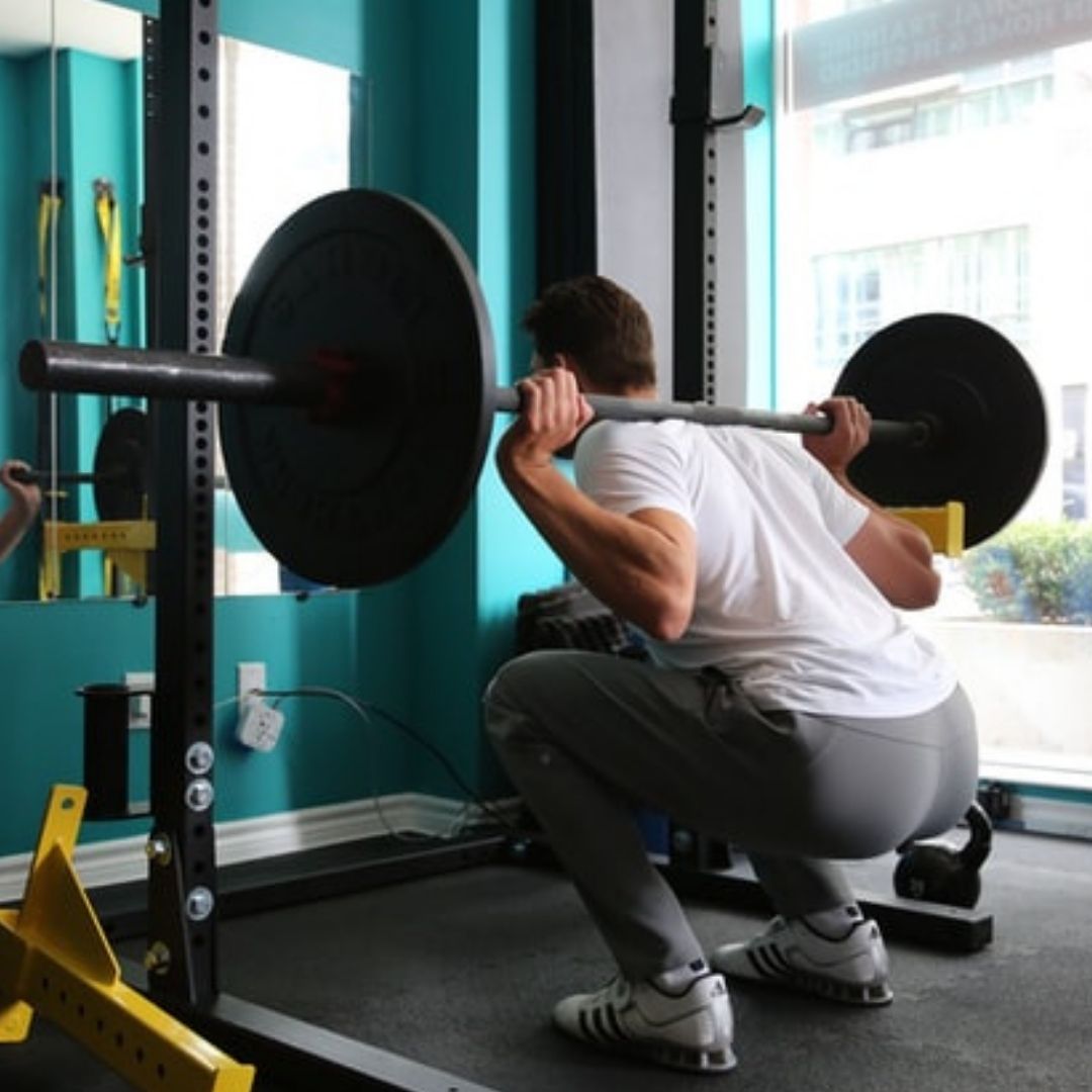 An athlete holding a deep barbell back squat inside a squat rack