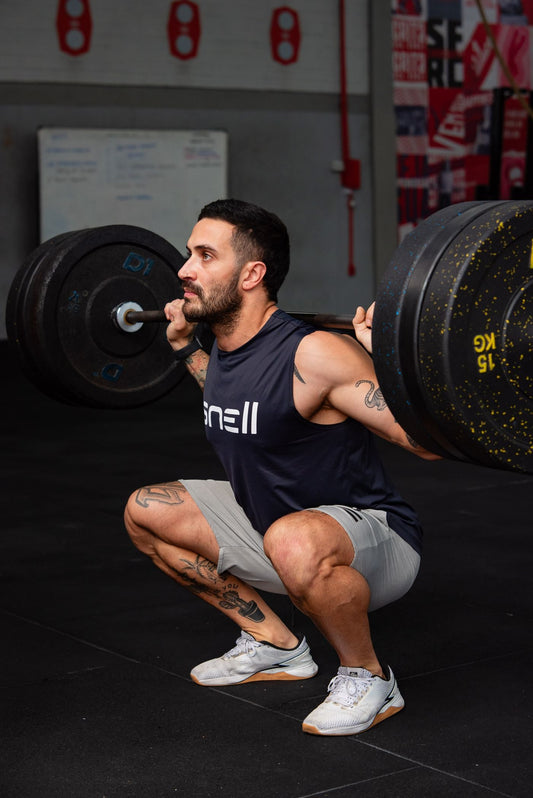 Male athlete performing a heavy barbell back squat inside a gym