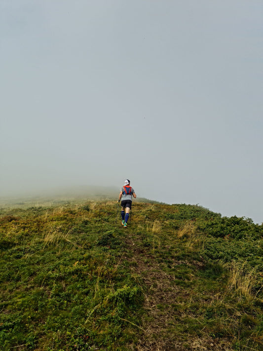 Solo trail runner climbing a misty grassy hill, symbolizing calm persistence during a difficult run