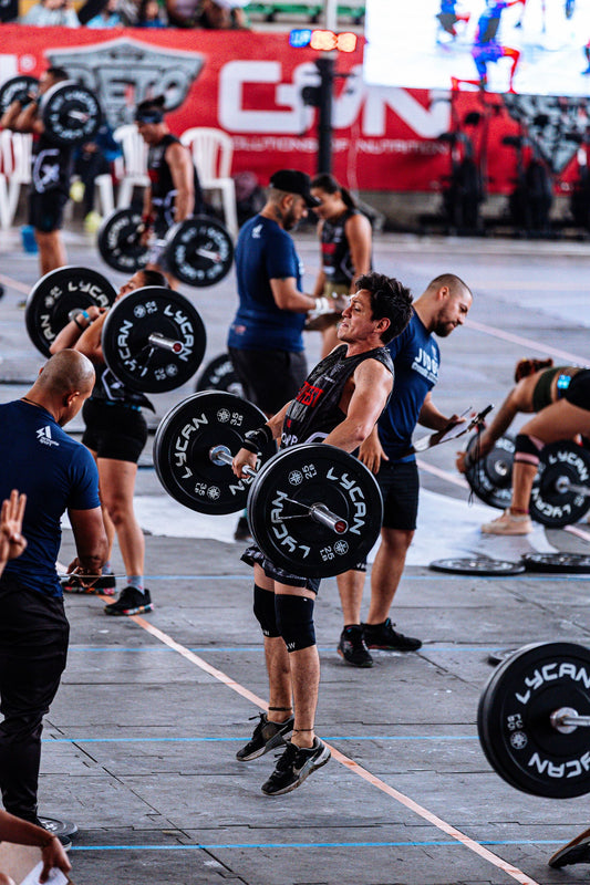 Functional fitness athletes lifting barbells on a judged competition floor