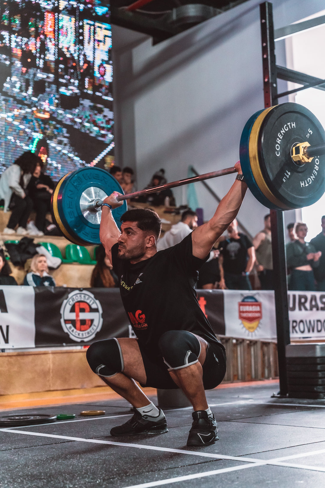 An athlete catches a loaded barbell overhead in a partial squat inside a functional fitness gym.