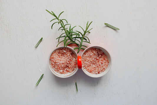 Coarse pink Himalayan salt and fresh rosemary in bowls on a table