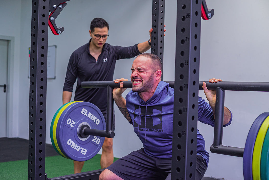 Strength coach supervising a man performing a barbell squat in a gym