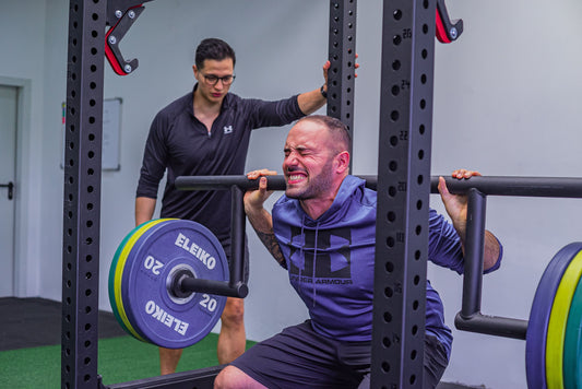 Strength coach supervising a man performing a barbell squat in a gym