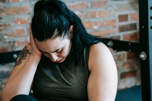 Woman sitting on a gym floor near exercise equipment, looking tired and stressed