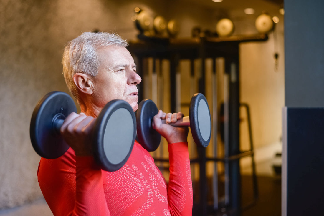 Older man lifting dumbbells at a gym, illustrating strength training across the lifespan